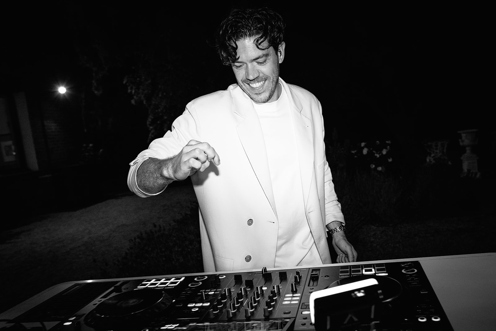Josh Parish, founder of Married to the Groove, smiling behind the decks in a white jacket