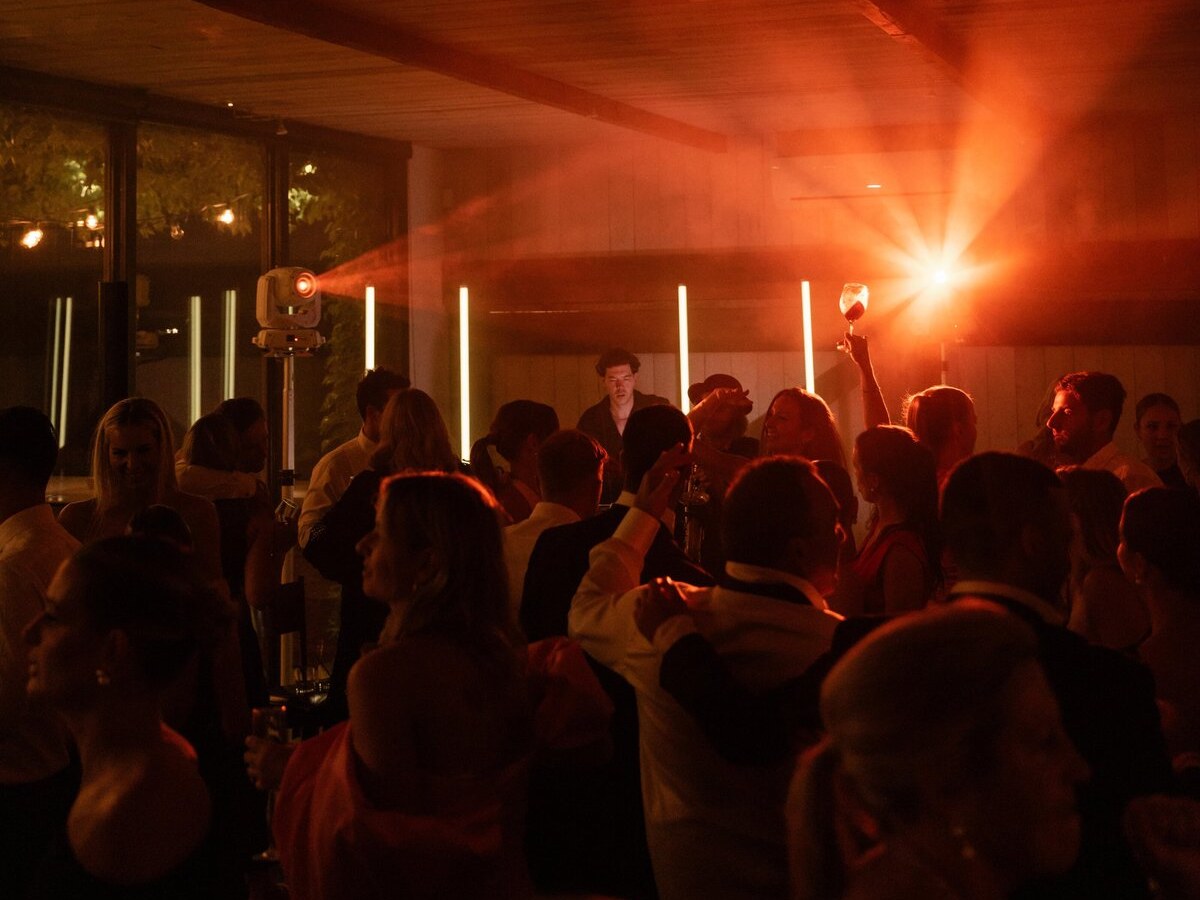 Packed wedding dancefloor under tube lighting, moving heads and haze